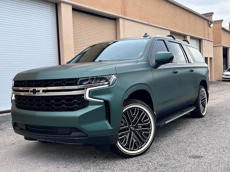 the front end of a green suv parked in front of a building with garage doors