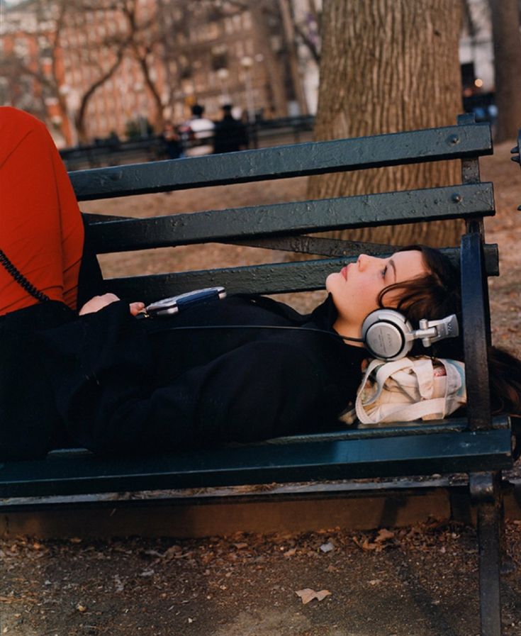 a woman with headphones laying on a bench