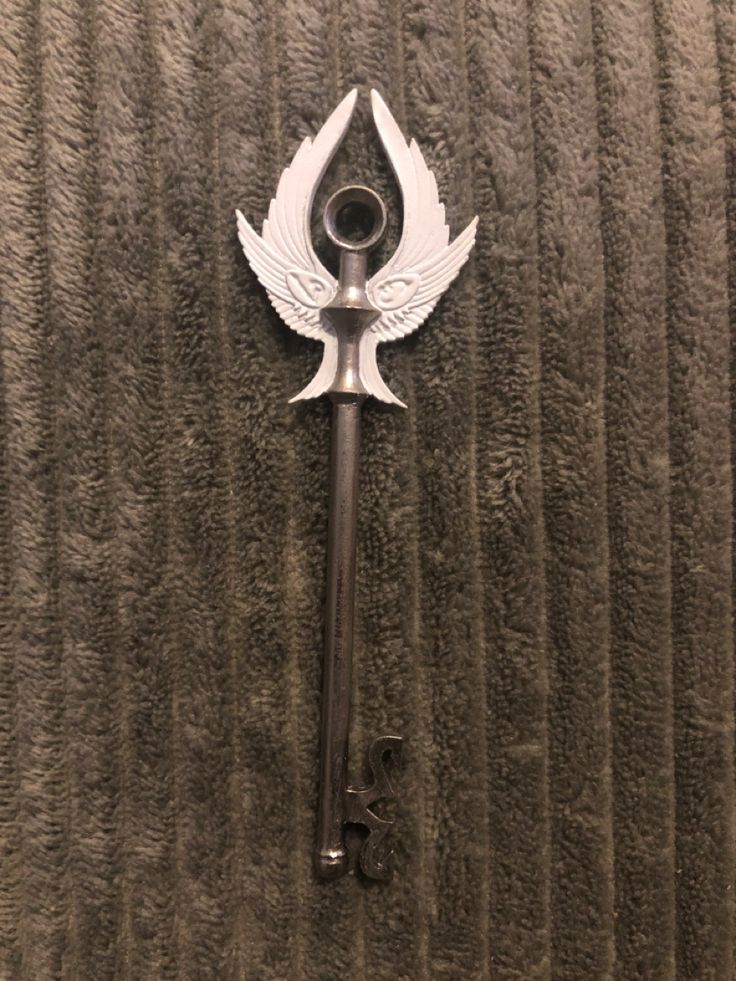 a metal key with wings on it hanging from the wall in front of a towel