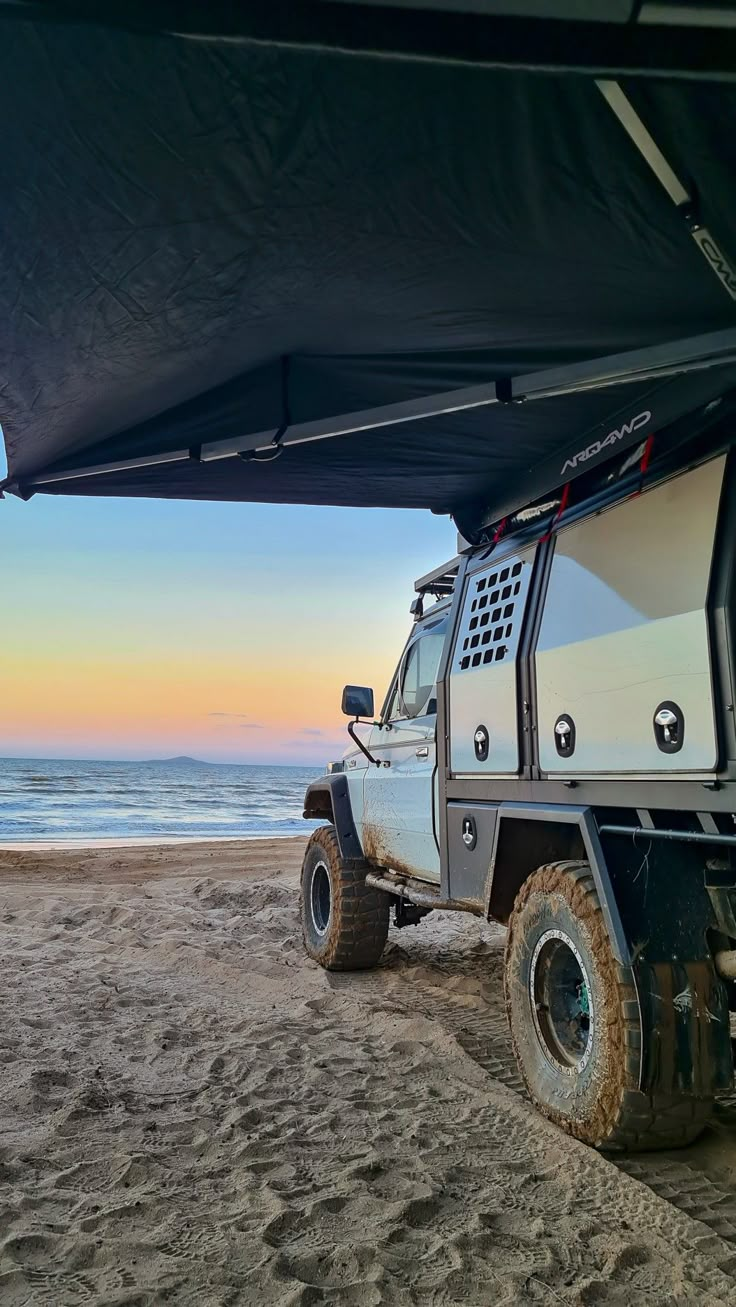 a white truck parked on top of a sandy beach next to the ocean at sunset