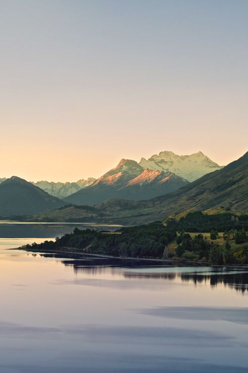 a lake surrounded by mountains and trees in the distance with water below it at sunset