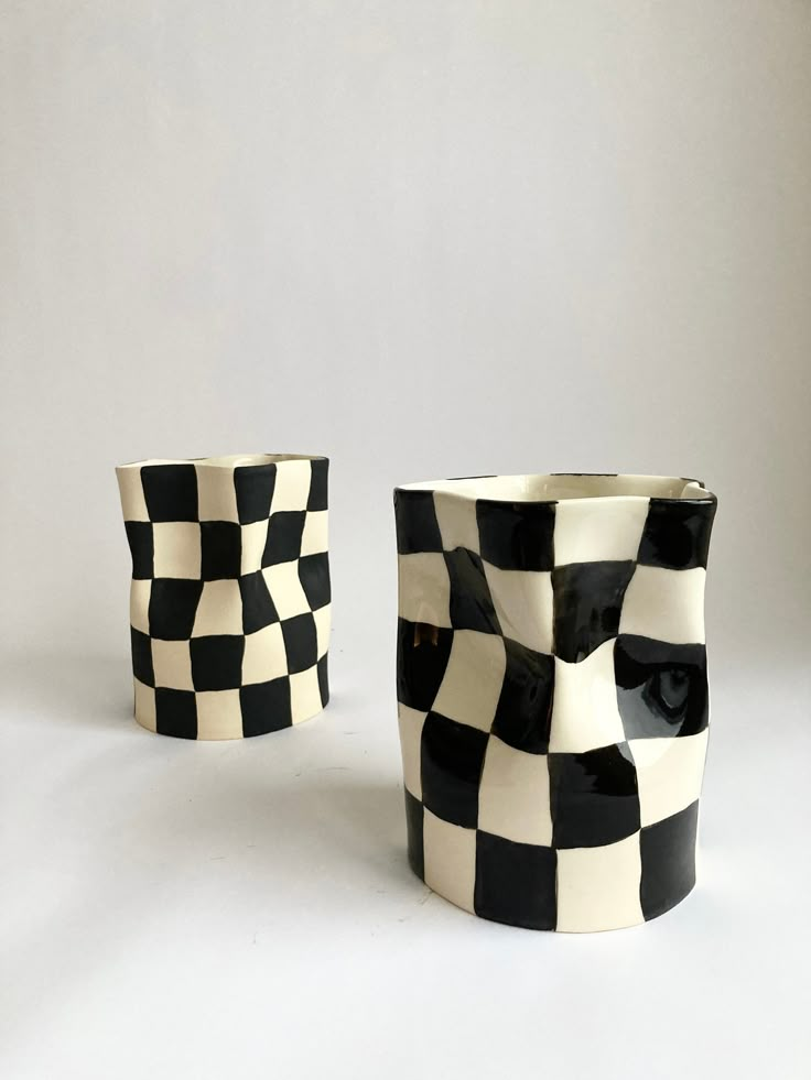 two black and white checkered cups sitting next to each other on a white surface