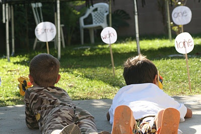 two young boys laying on the ground in front of some lawn signs with one boy holding an orange frisbee