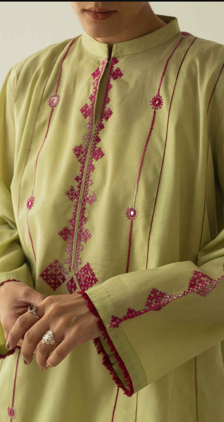 a woman wearing a green dress with pink embroidery on it