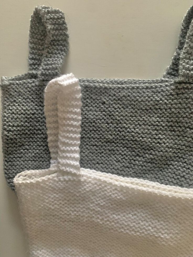 two knitted bags sitting on top of each other next to a white bag with handles