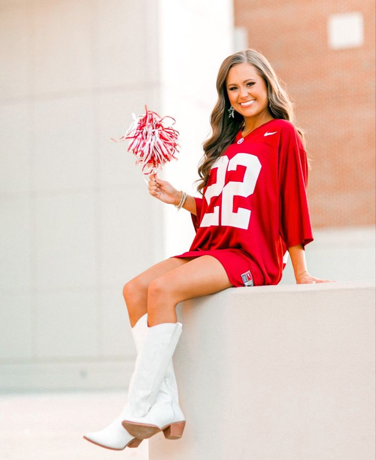 a beautiful young woman sitting on top of a cement wall holding a cheerleader pom pom