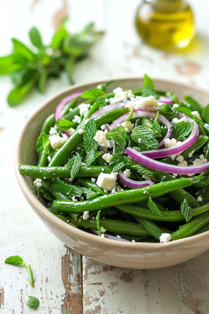 a bowl filled with green beans, onions and feta on top of a wooden table