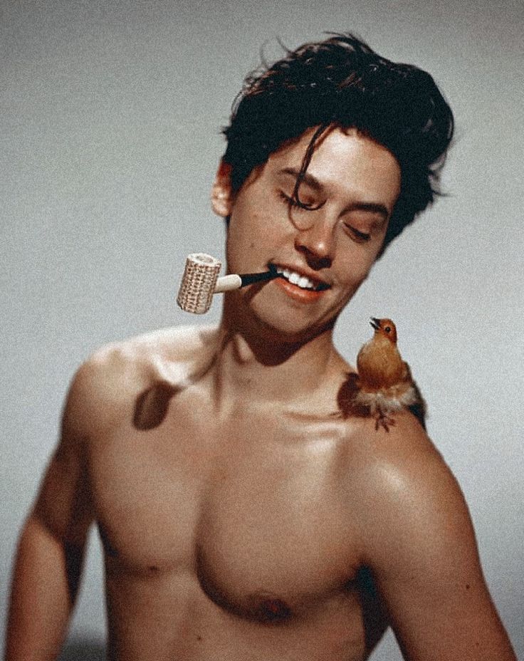 a shirtless man brushing his teeth with an electric toothbrush and bird on his shoulder