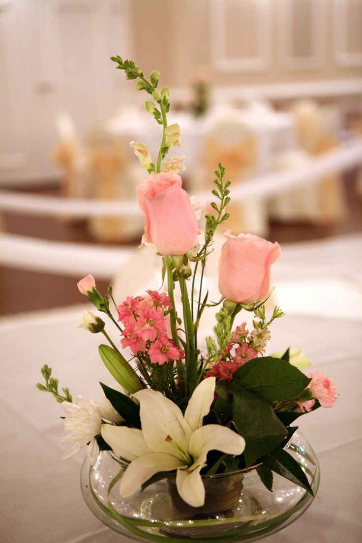 a vase filled with pink roses and white lilies on top of a table in a restaurant