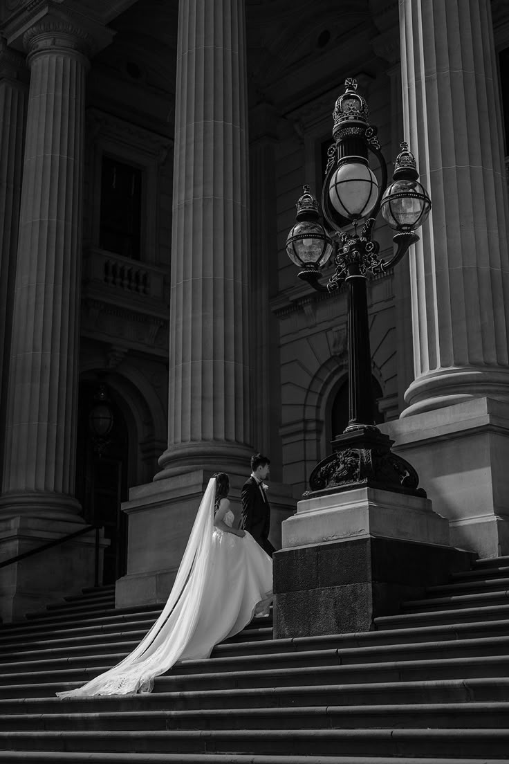 a bride and groom standing on the steps of an old building in black and white