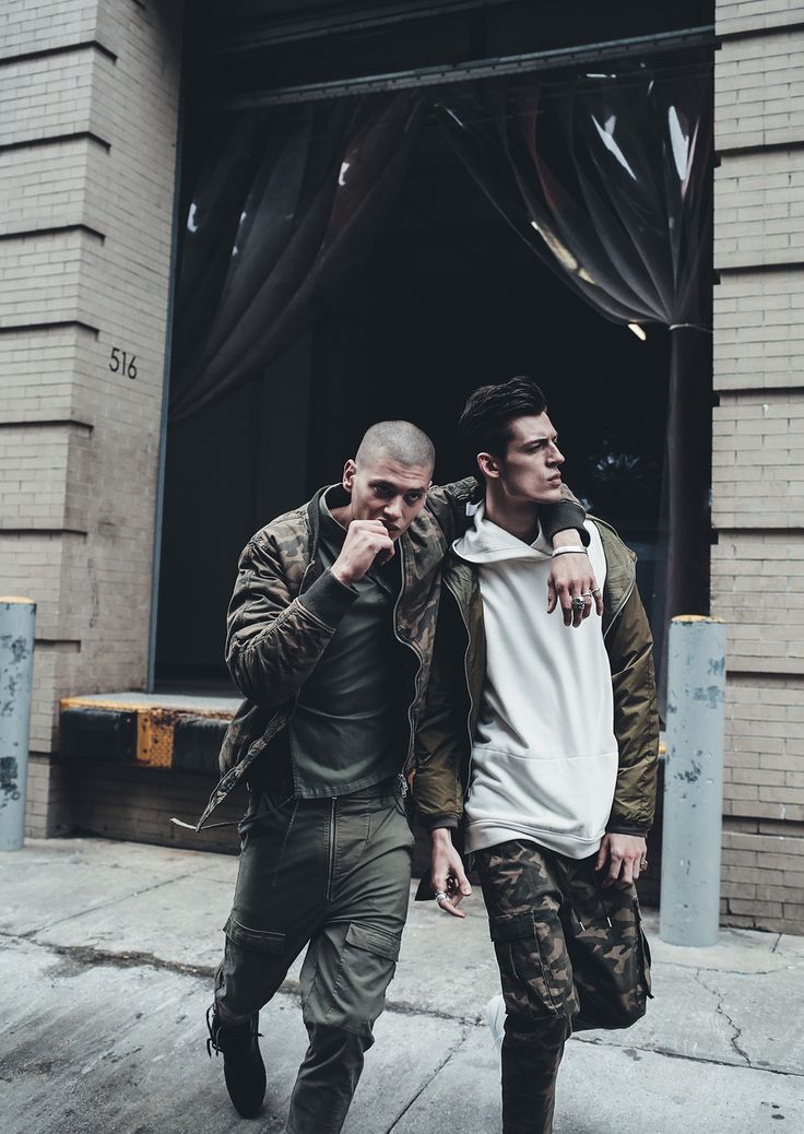 two men are walking down the street in front of a building and one is holding his arm around another man's shoulder