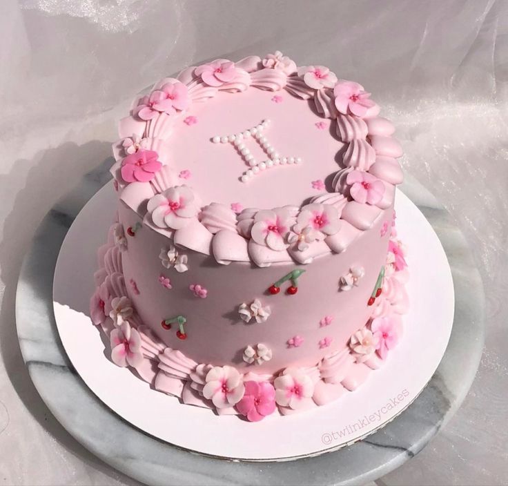 a pink cake decorated with flowers and the letter t on top is sitting on a plate