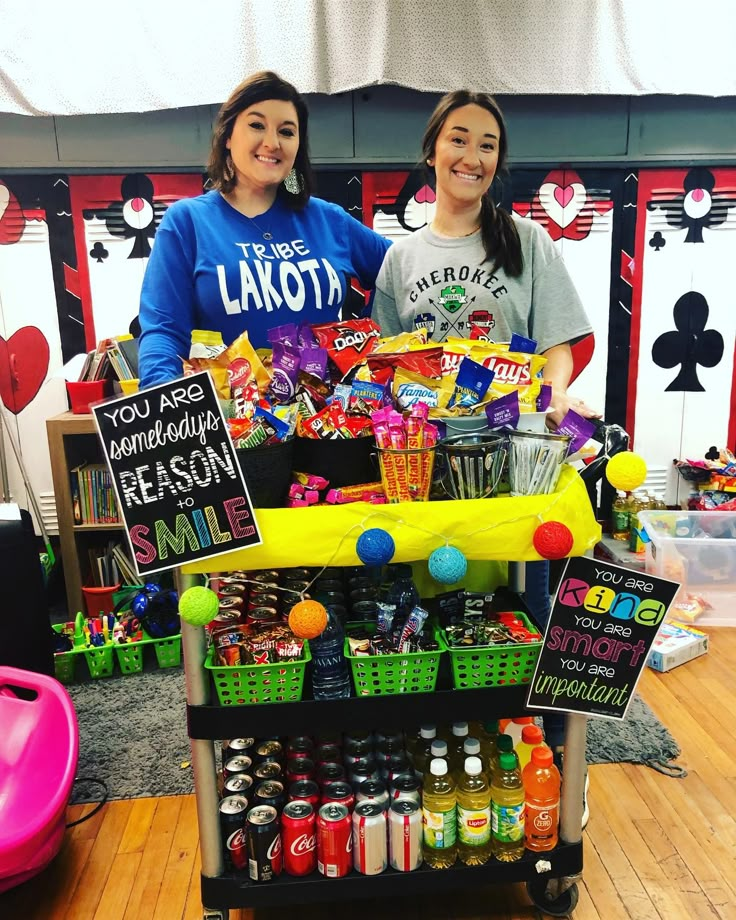 two women standing behind a table filled with drinks and snacks for an event or party