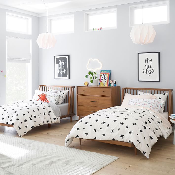 two children's beds in a white room with wooden furniture and artwork on the walls