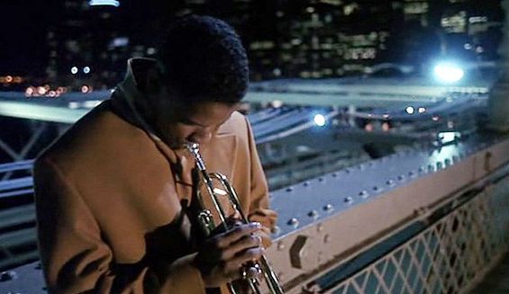 a man holding a trumpet on top of a bridge in the city at night time