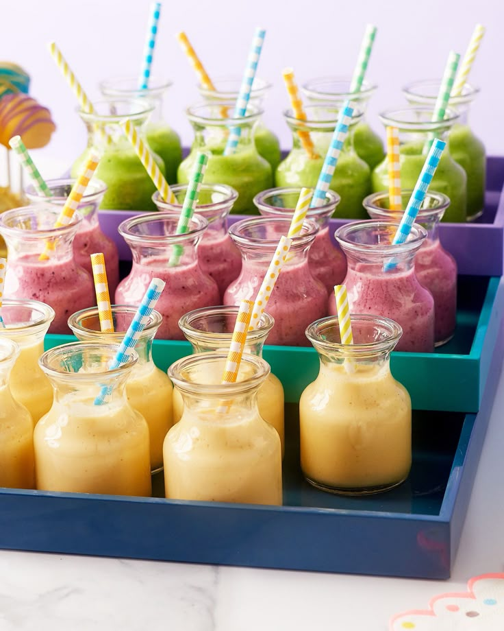 there are many drinks in small glass jars on the tray with colorful straws and striped paper straws