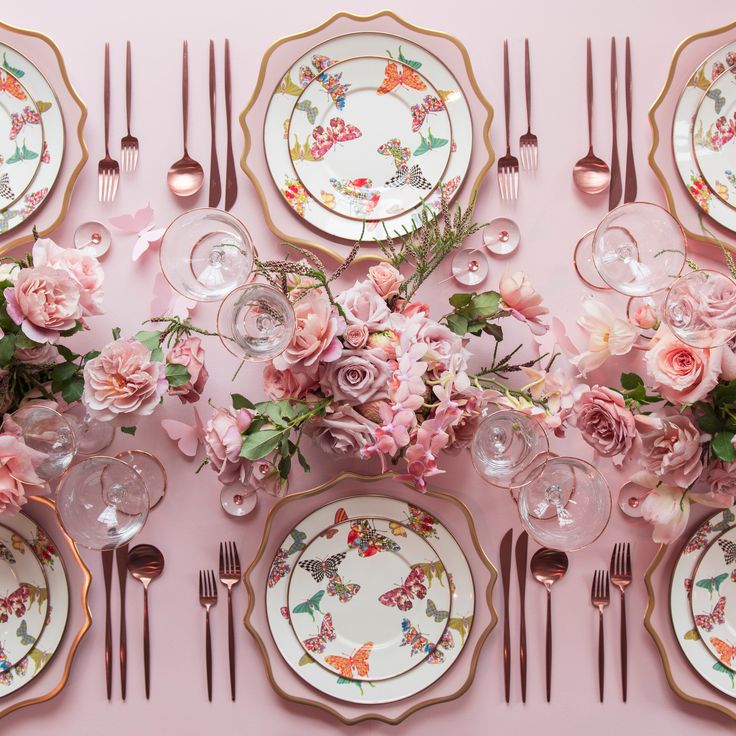 the table is set with pink flowers and gold trimmings, plates and silverware