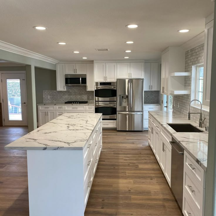 a large kitchen with white cabinets and marble counter tops, along with stainless steel appliances