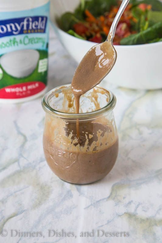 a spoon is pouring peanut butter into a jar with salad in the background and a can of yogurt behind it