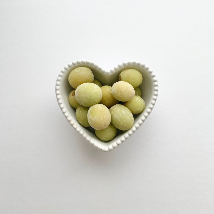 a heart shaped bowl filled with green olives on top of a white countertop