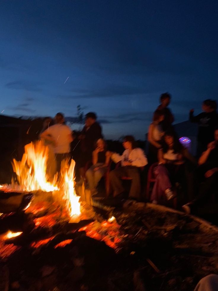 a group of people sitting around a campfire at night with the sky in the background