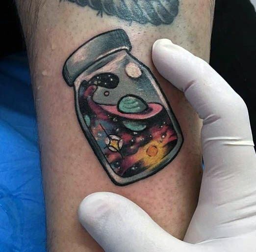 a person with a tattoo on their arm holding up a jar filled with colorful liquid