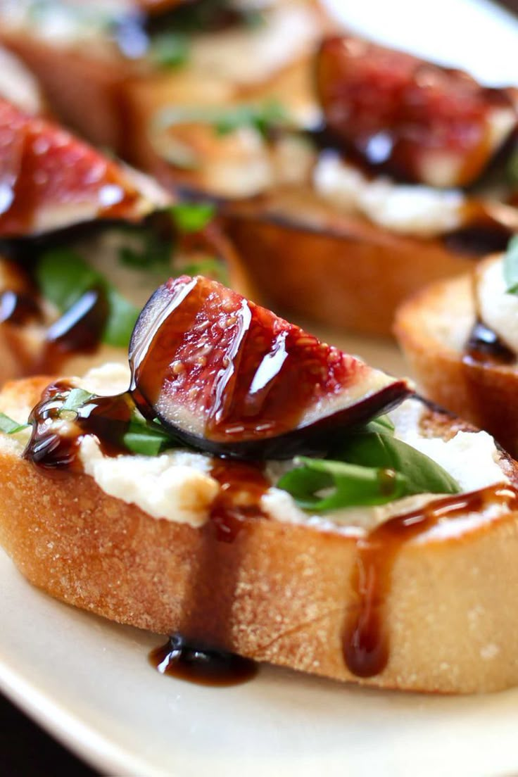 slices of bread topped with figs, cheese and sauce on a white platter