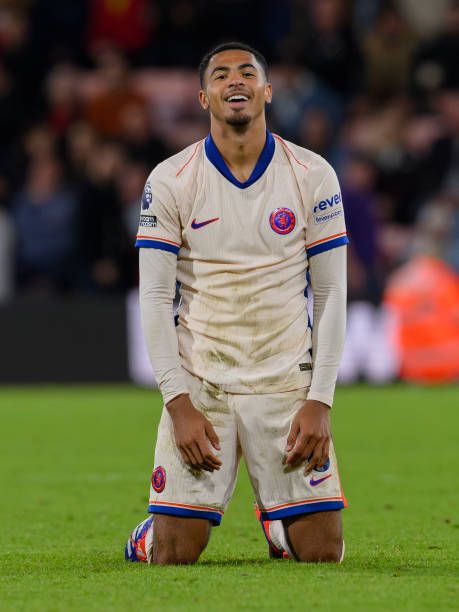 a soccer player is sitting on the field with his hands in his pockets and smiling