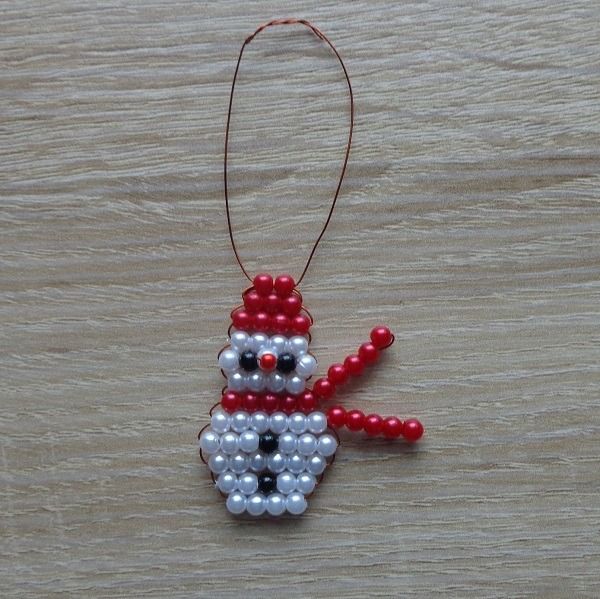 a beaded snowman ornament hanging on a wooden table