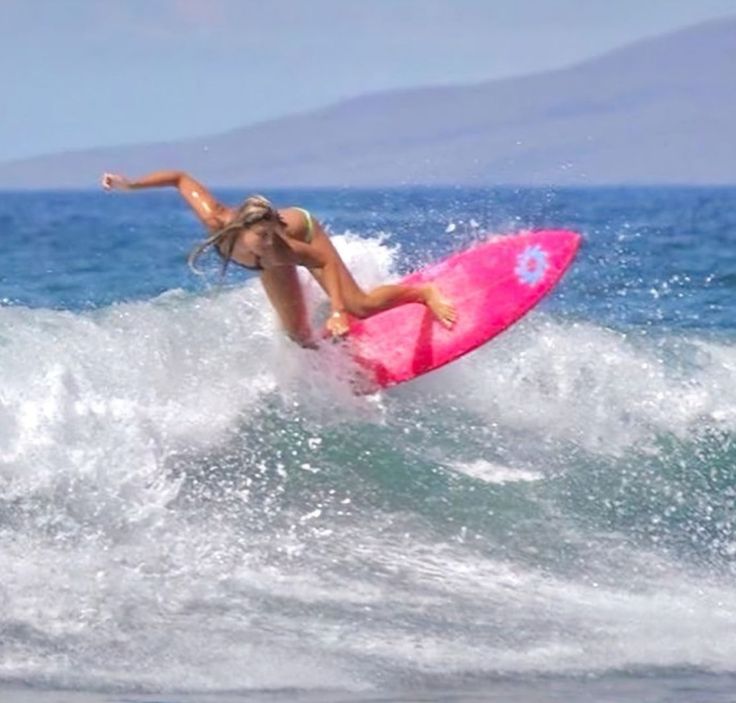 a woman riding a pink surfboard on top of a wave