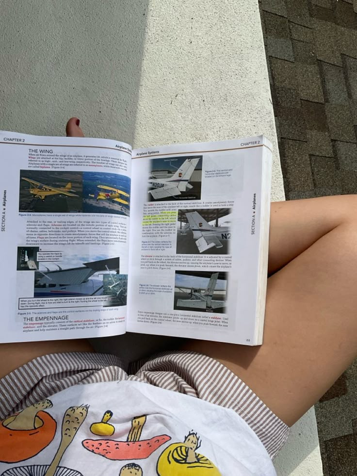 a person laying on the ground reading a book with an airplane in it's pages