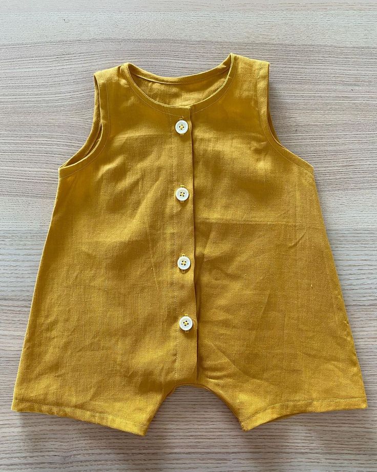 a baby's yellow dress with buttons on the front and bottom, sitting on a wooden surface