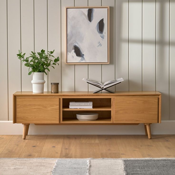 a wooden entertainment center with books and plants on it in front of a white wall