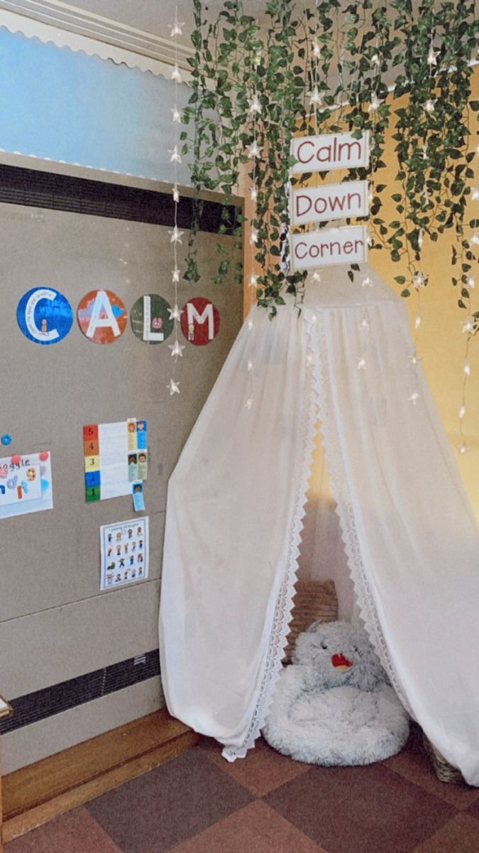 a room with a bed and plants hanging from the ceiling, in front of a bulletin board that says calm down corner