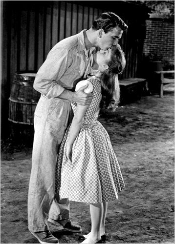 an old black and white photo of a man kissing a woman on the cheek in front of a barn