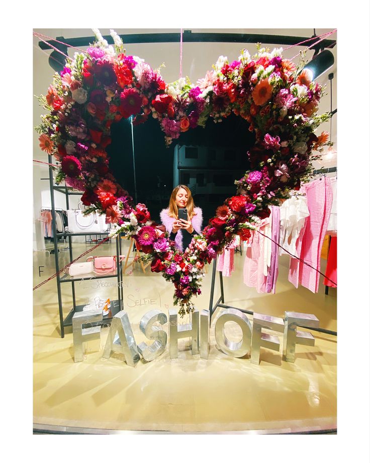 a woman standing in front of a heart shaped sign with flowers on it that says fashion