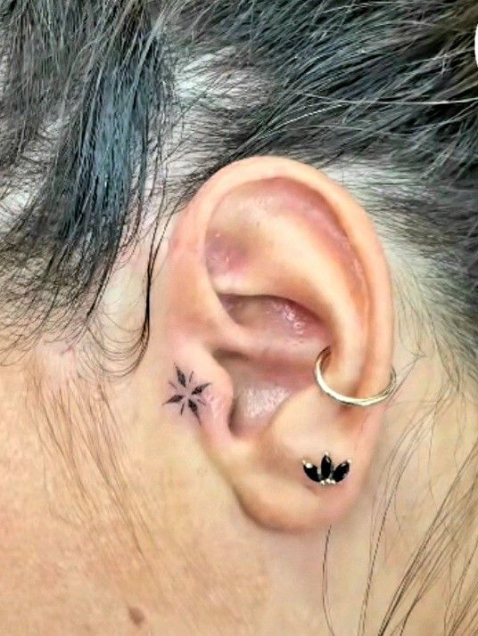 a woman's ear has a small flower tattoo on it