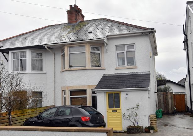 a black car parked in front of a white two story house with a yellow door