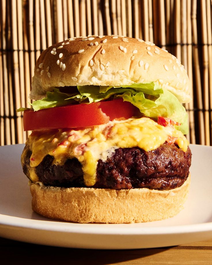 a cheeseburger with tomatoes, lettuce and tomato on a white plate