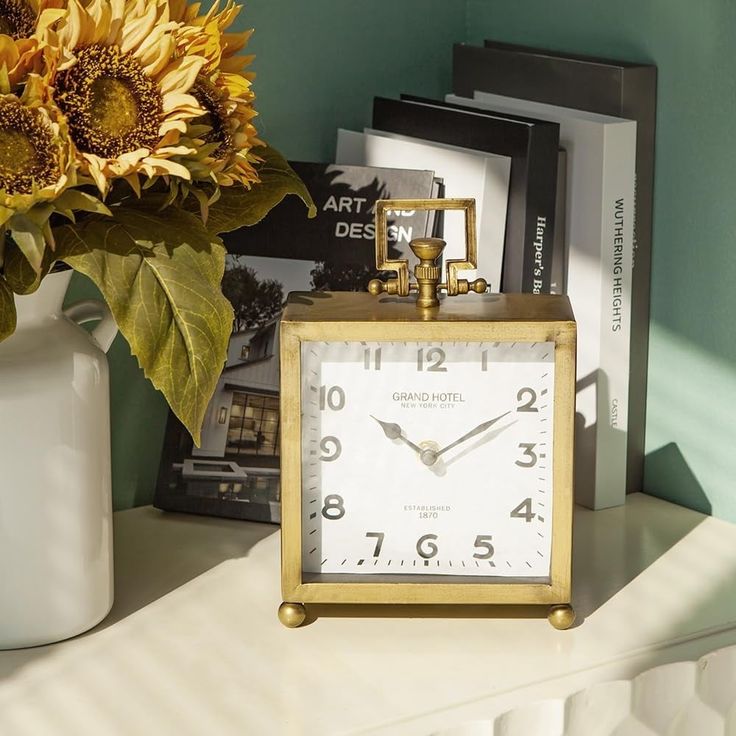 a clock sitting on top of a table next to a vase with sunflowers