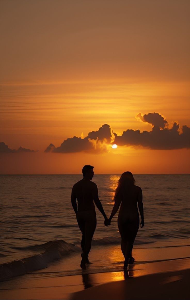 two people walking on the beach holding hands as the sun sets in the distance behind them