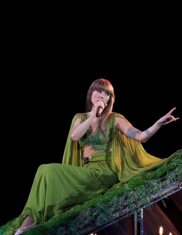 a woman in a green dress is holding her hand out and singing into a microphone