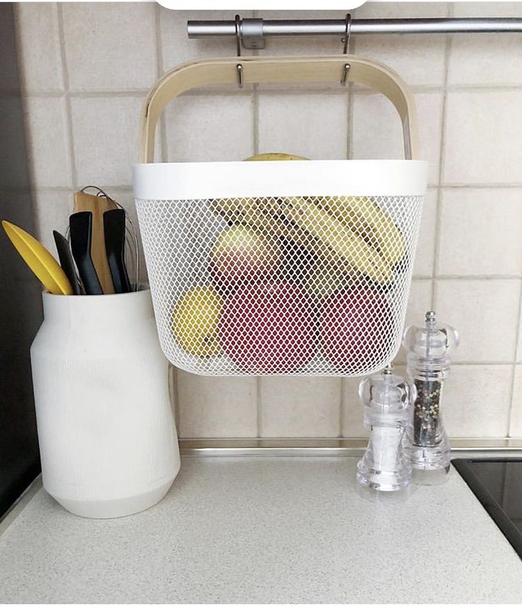 a white basket filled with fruit sitting on top of a counter next to a knife holder