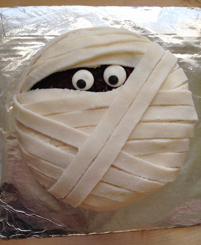 a wrapped up cake with eyes and bandages on it's face, sitting on aluminum foil