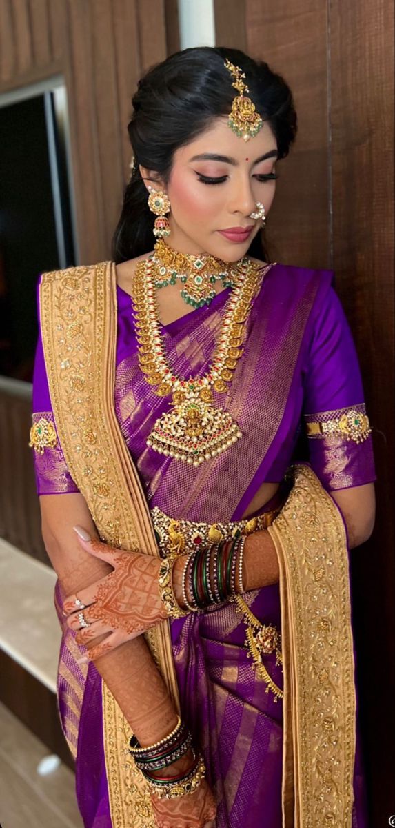 a woman in a purple and gold sari with jewelry on her neck, arms and hands