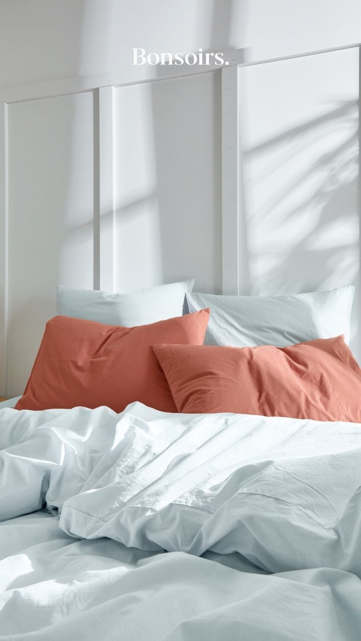 an unmade bed with white sheets and orange pillows