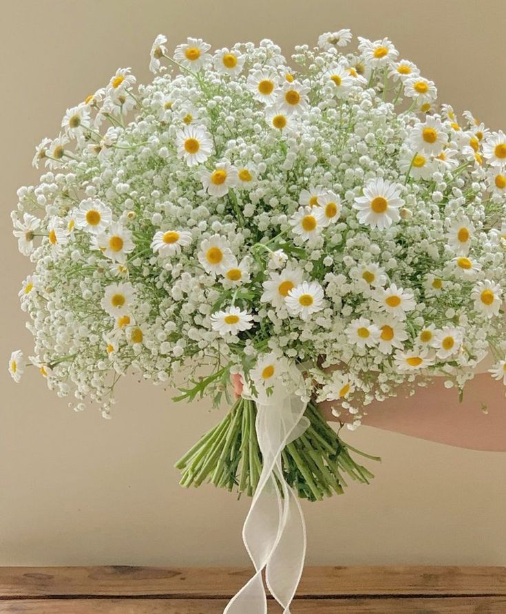 a bouquet of daisies and baby's breath tied to a white ribbon on a table