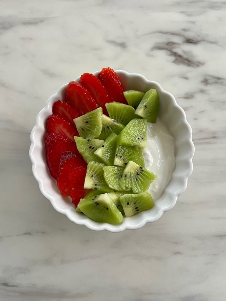 sliced kiwis and strawberries in a white bowl on a marble countertop