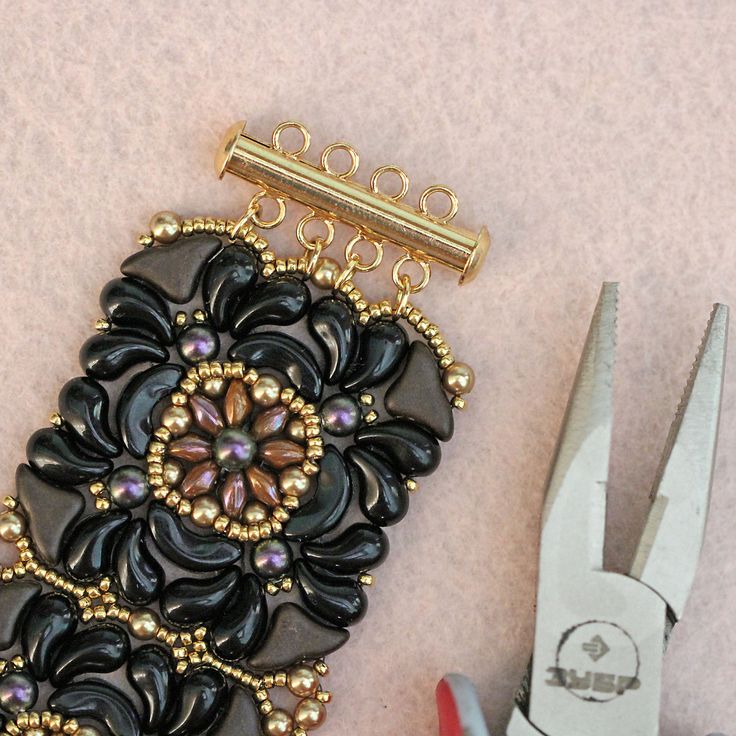 a pair of scissors and some beading on a pink table next to a piece of jewelry