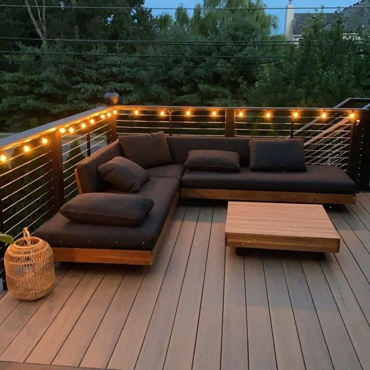 a couch sitting on top of a wooden deck next to a table and lights above it